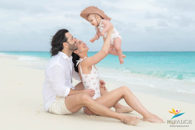 12-Family-Photos-in-Turks-and-Caicos family sitting on the beach holding up their baby