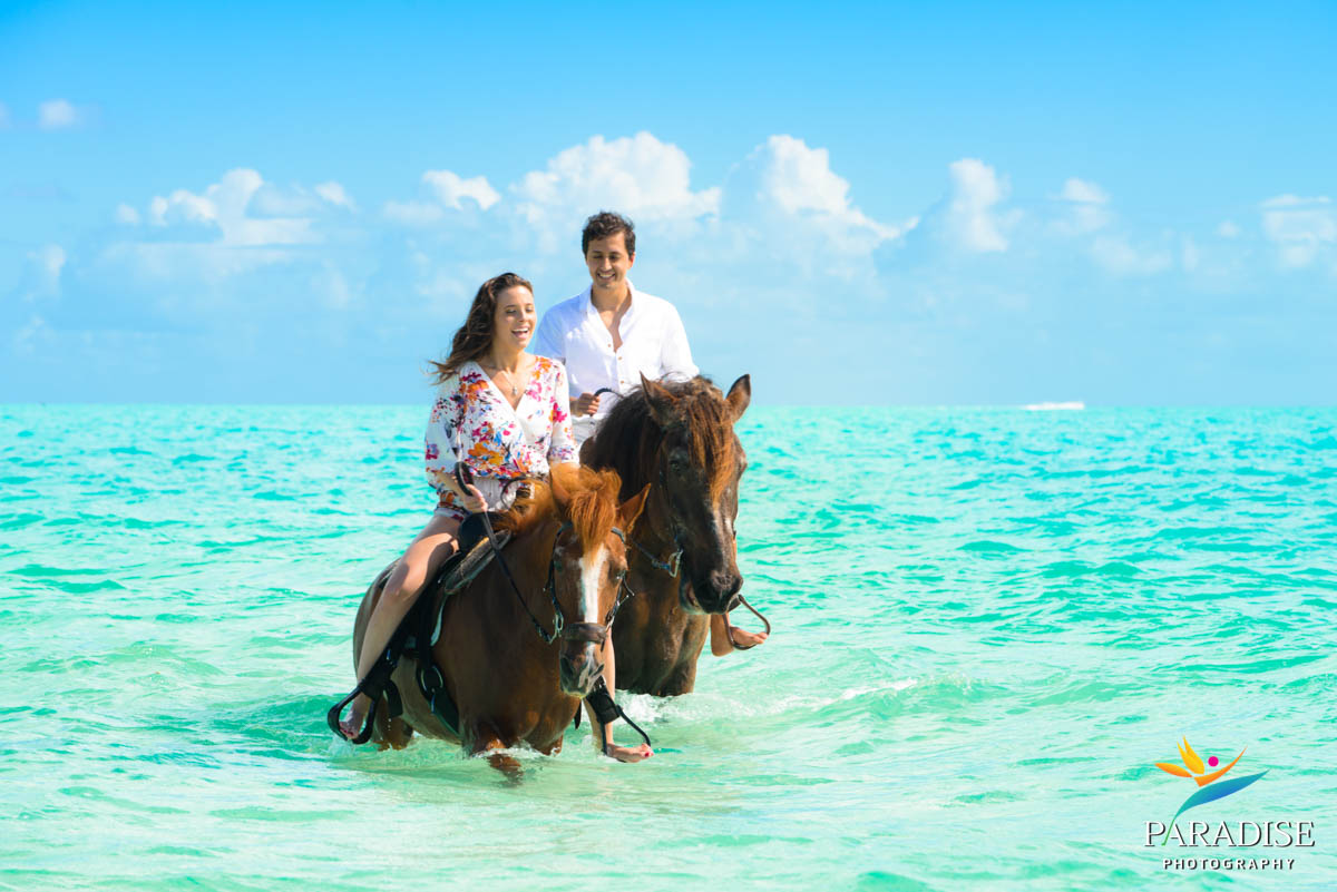 Couple riding horses through crystal-clear waters in Turks and Caicos