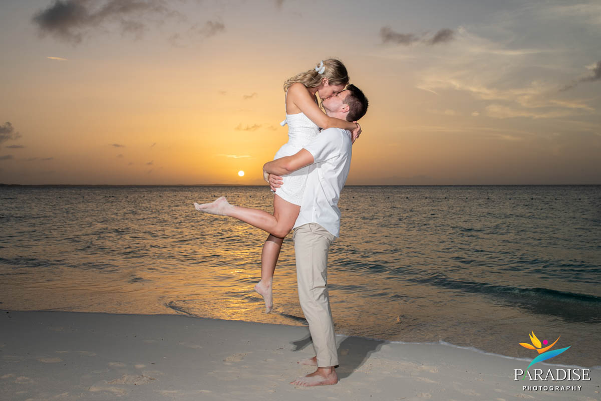 Man lifting and kissing his fiancée as sun sets over ocean