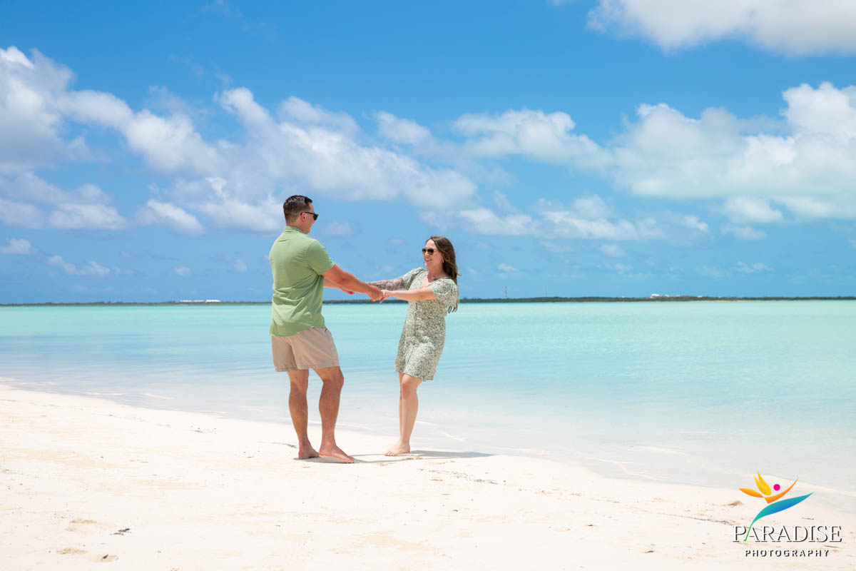 Couple laughing and spinning on white sand in front of clear turquoise sea