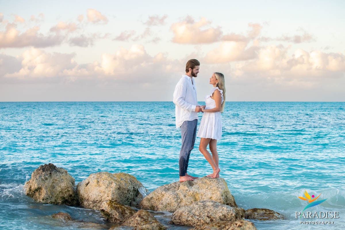 Couple standing barefoot on rocks, surrounded by crashing waves