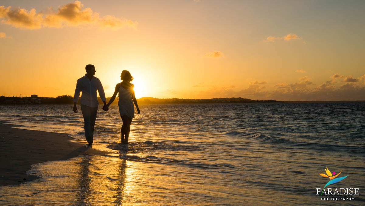 Couple silhouetted holding hands along shoreline at sunset