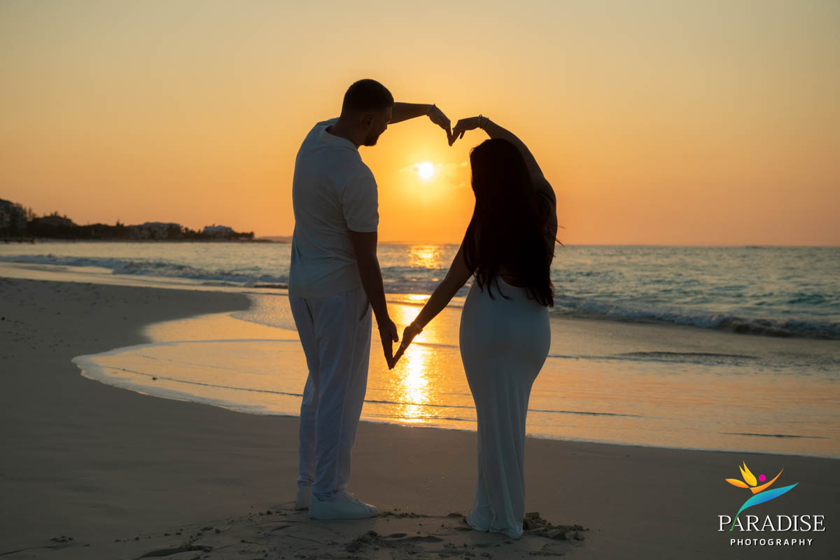 Couple forms heart shape with hands during glowing beach sunset
