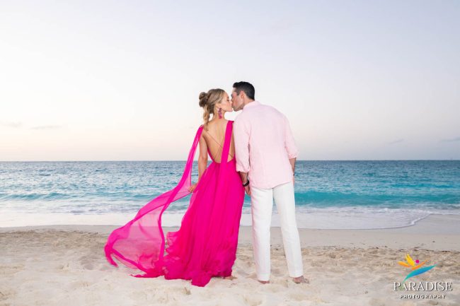 sunset-kiss-pink-dress Couple in a pink dress and light shirt kissing at sunset on Grace Bay Beach