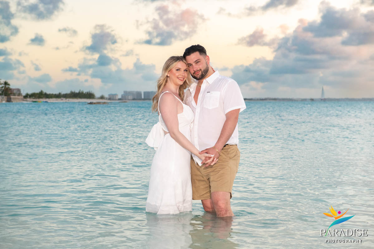 Couple standing in the water in matching white, embracing at dusk
