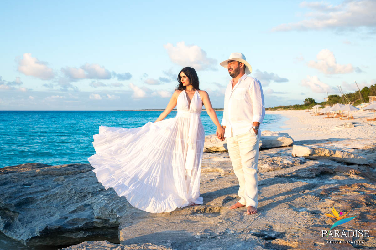 Woman’s dress flowing in breeze as couple stands on rocky shore