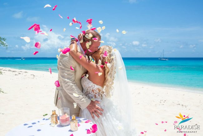 petal-kiss-on-beach Bride and groom kiss as rose petals fall on Grace Bay beach
