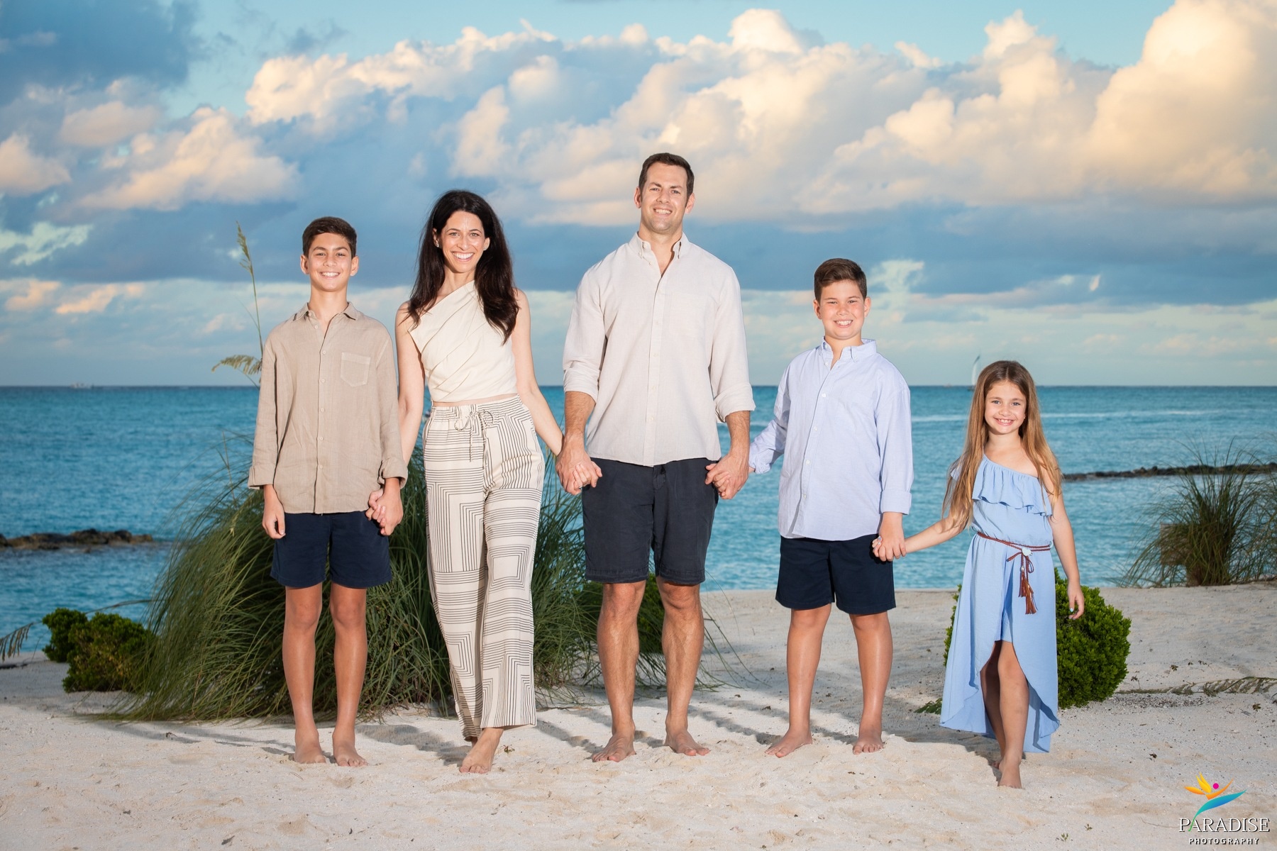 A beautiful family standing together for a portrait with calm blue water behind them