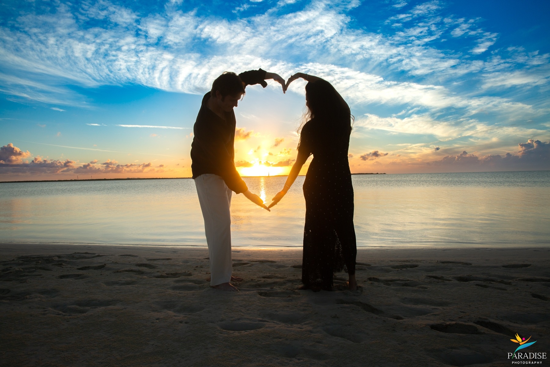 A beautiful family forming a heart shape silhouette against a glowing sunset beach sky