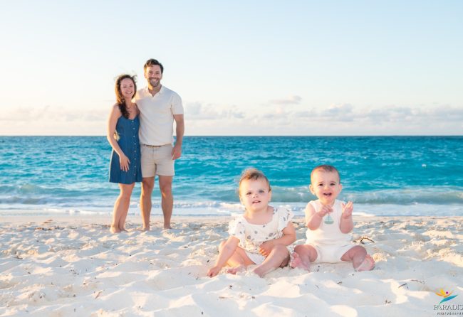 Parents standing behind twin toddlers on the shoreline in Turks and Caicos