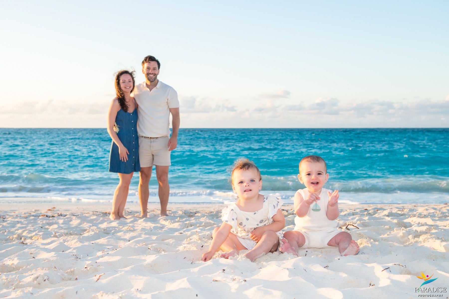 Parents standing behind twin toddlers on the shoreline in Turks and Caicos