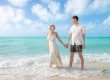 Bride and groom holding hands and walking together through the shallow ocean water