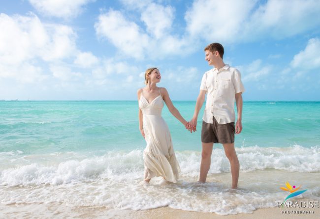 turks-and-caicos-engagement-photographer-couple-walking-shoreline-waves Bride and groom holding hands and walking together through the shallow ocean water