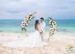 Bride and groom at a gold floral arch with lace train spread across the sand on a Turks and Caicos beach