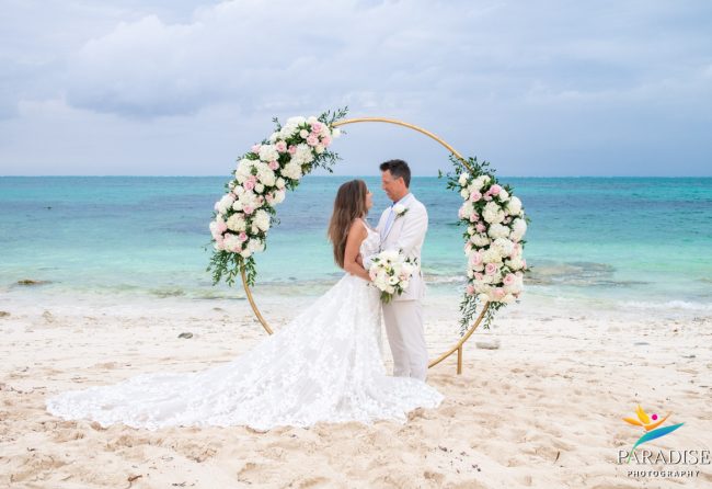 Bride and groom at a gold floral arch with lace train spread across the sand on a Turks and Caicos beach