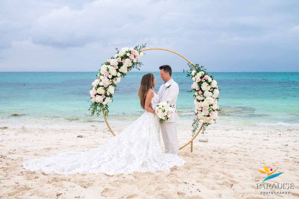 Bride and groom at a gold floral arch with lace train spread across the sand on a Turks and Caicos beach